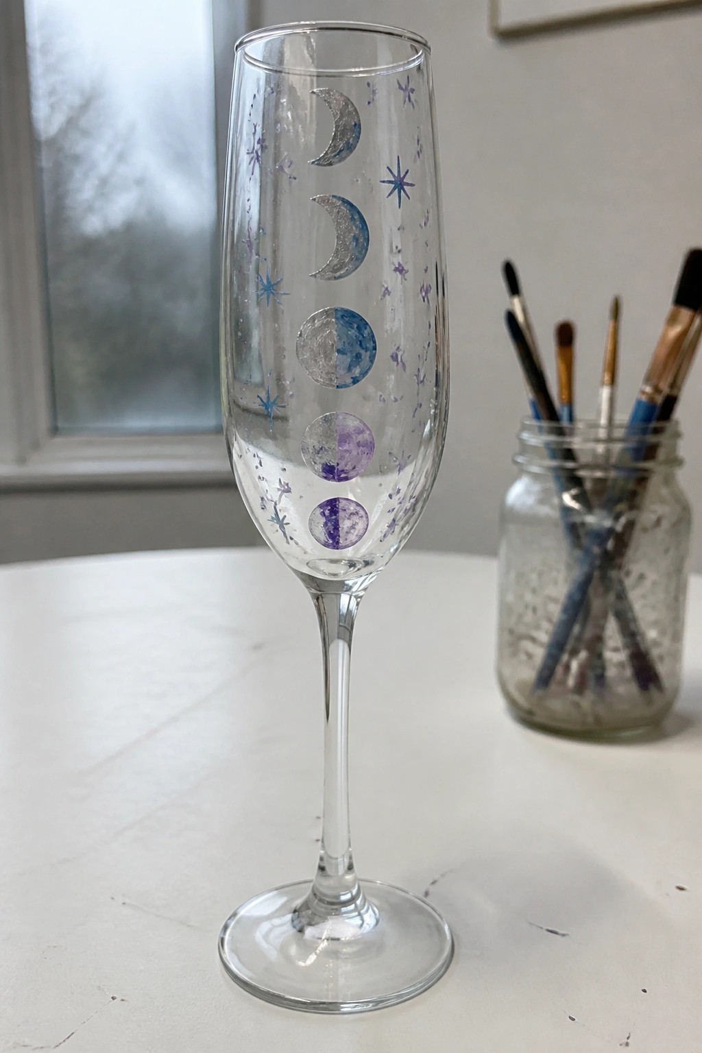 Champagne flute painted with moon phases in silver, blue, and purple plus stars