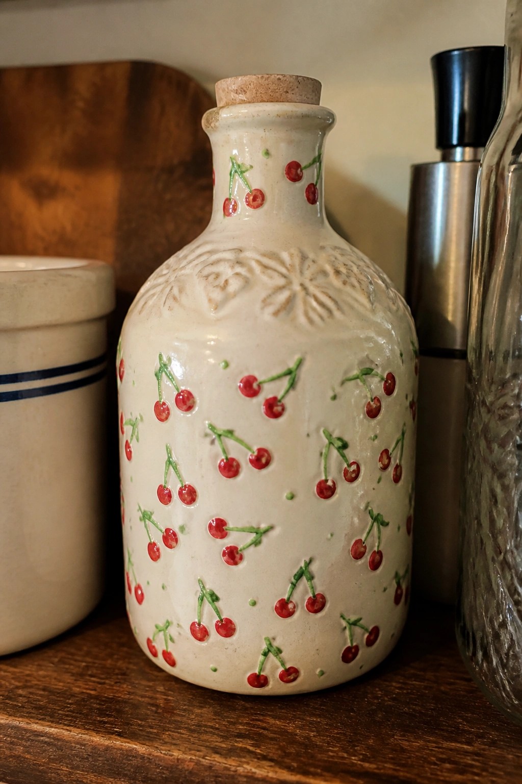 White ceramic bottle with red cherries, green stems, and cork stopper on wood.