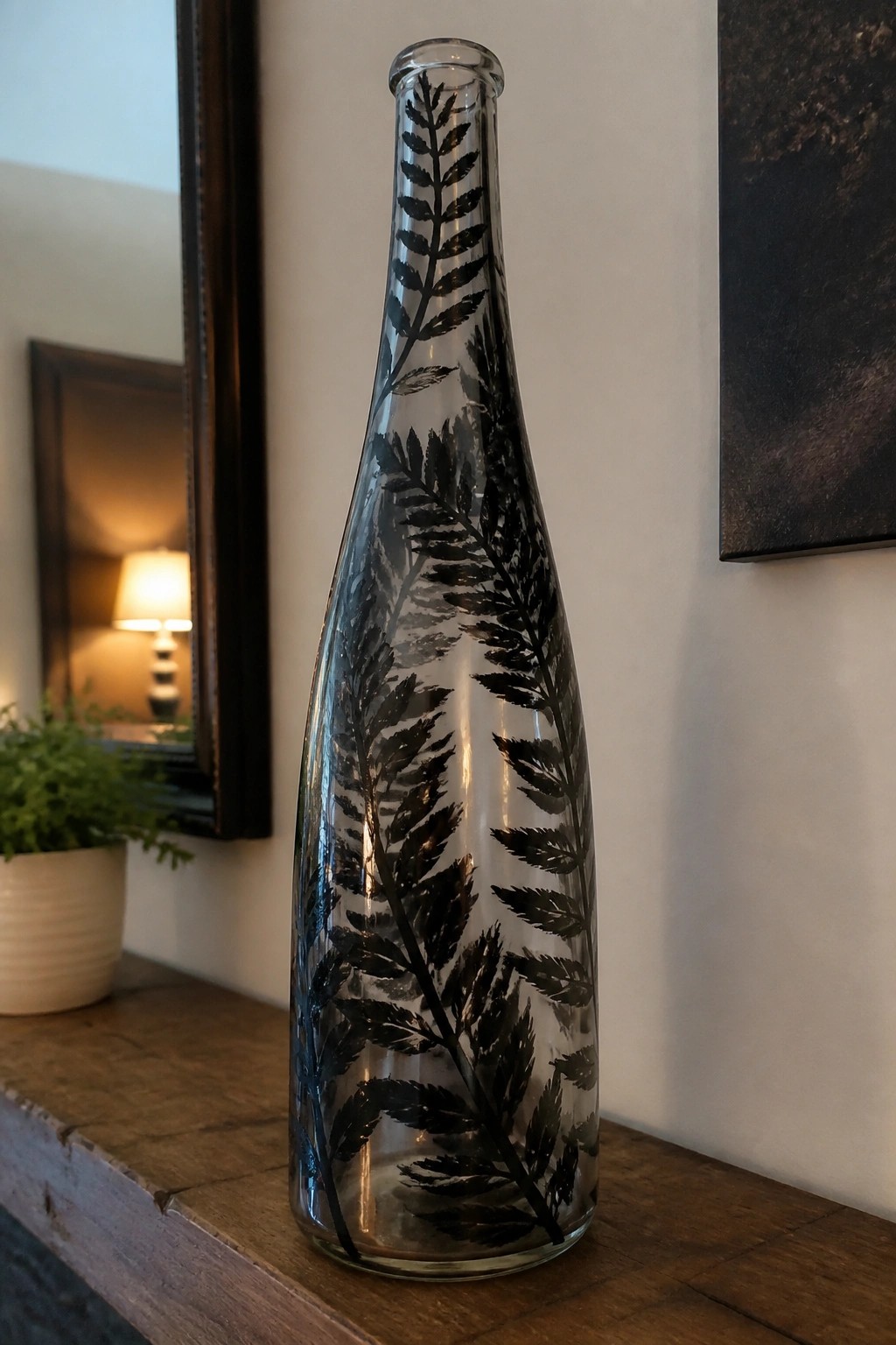 Tall glass bottle with black fern patterns on wooden surface