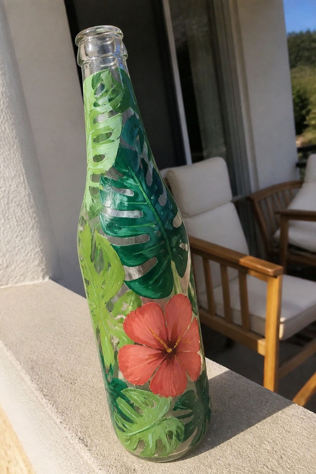 Tall glass bottle painted with green tropical leaves and red hibiscus flower on ledge