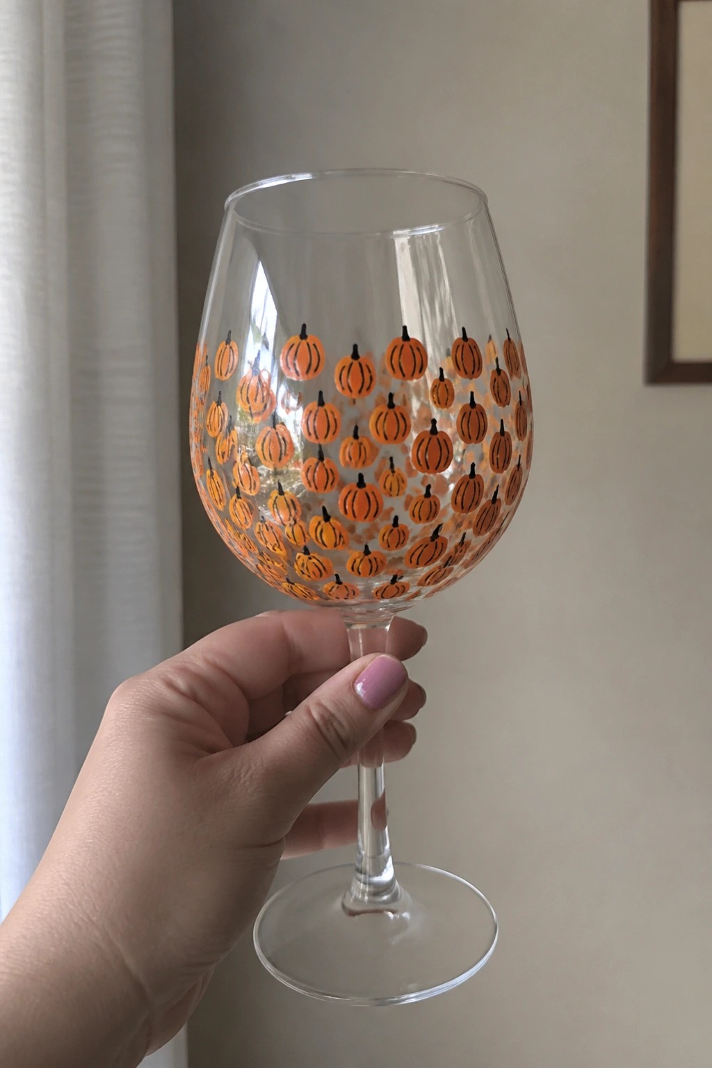 Hand holding wine glass painted with orange pumpkins and black stems.