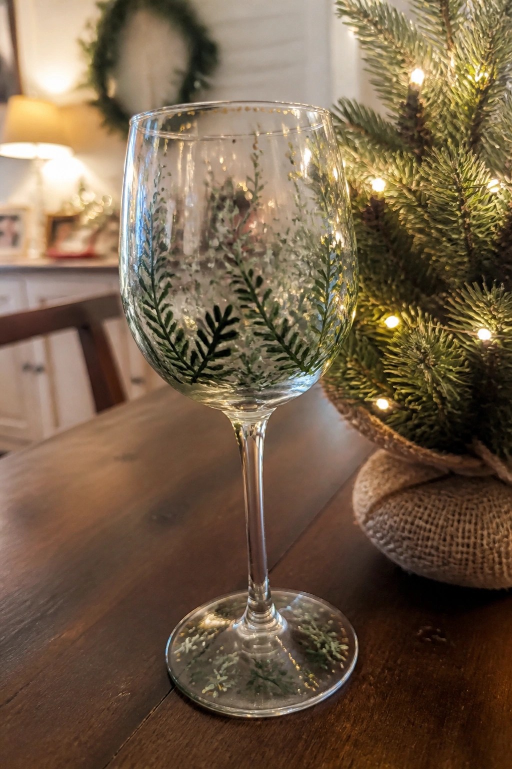 Stemmed wine glass with green fern designs and gold accents beside lit Christmas tree