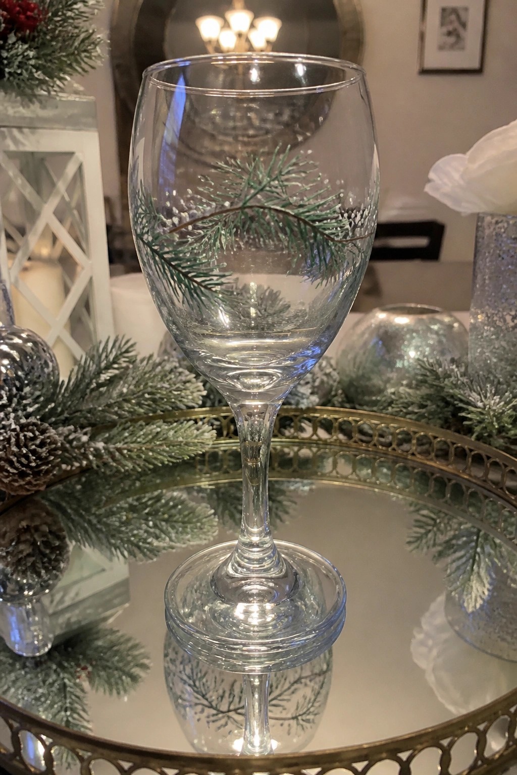 Stemmed wine glass with green pine design on gold-edged mirrored tray with holiday decor
