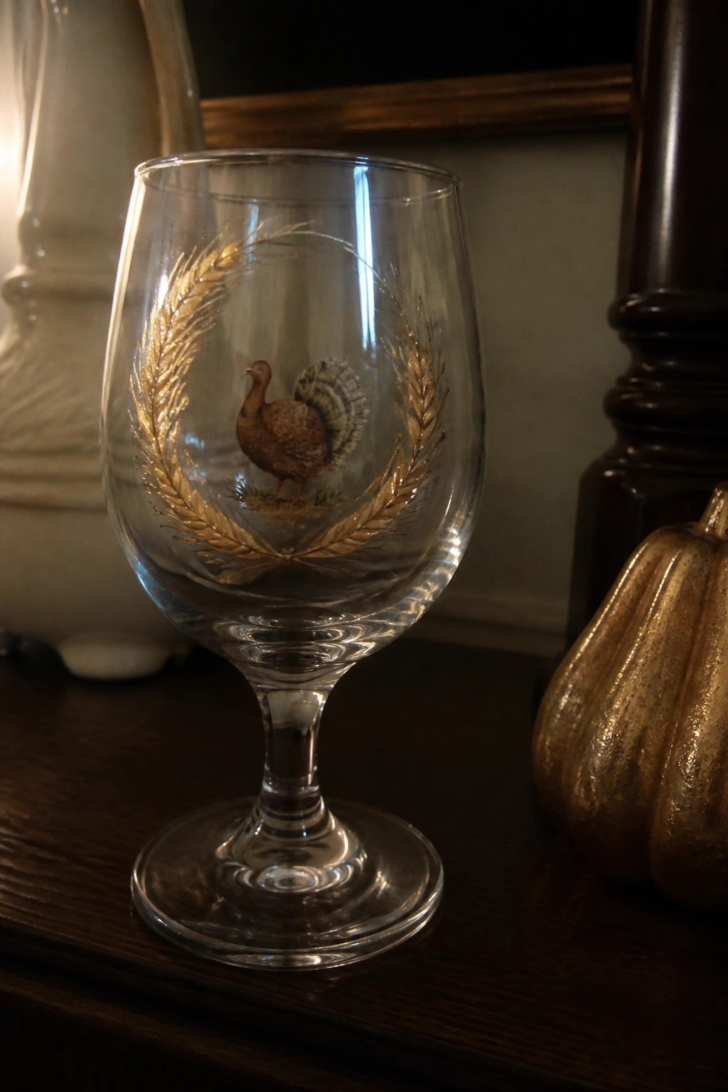 Clear glass goblet with brown turkey and gold wheat wreath beside gold pumpkin.