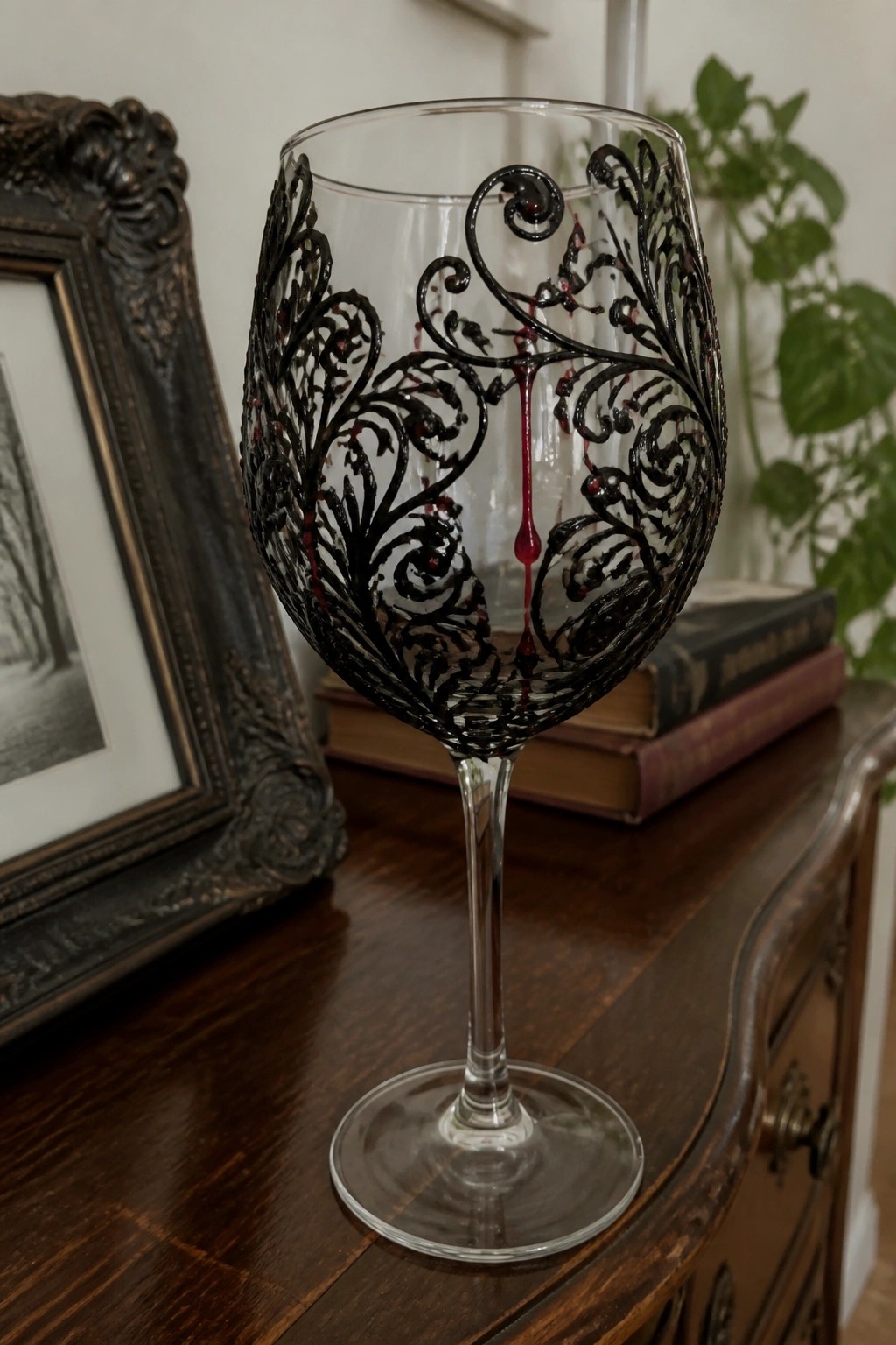 Ornate wine glass with black filigree patterns and dripping red liquid on wooden table