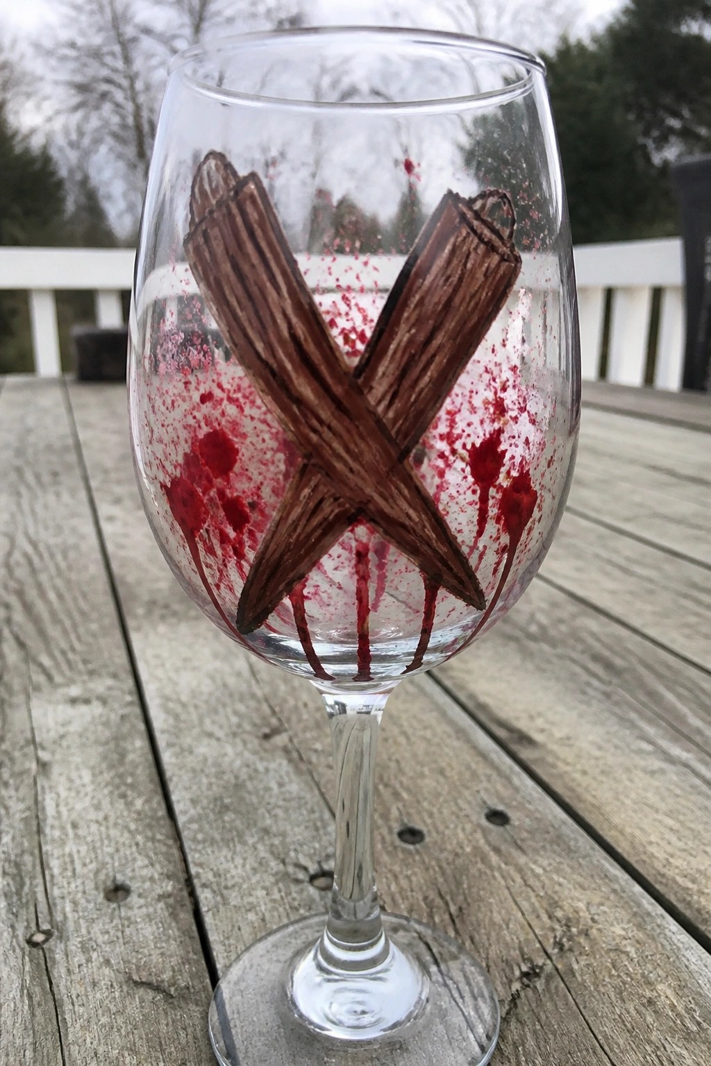 Wine glass with brown crossed logs and red paint splatters on wooden table