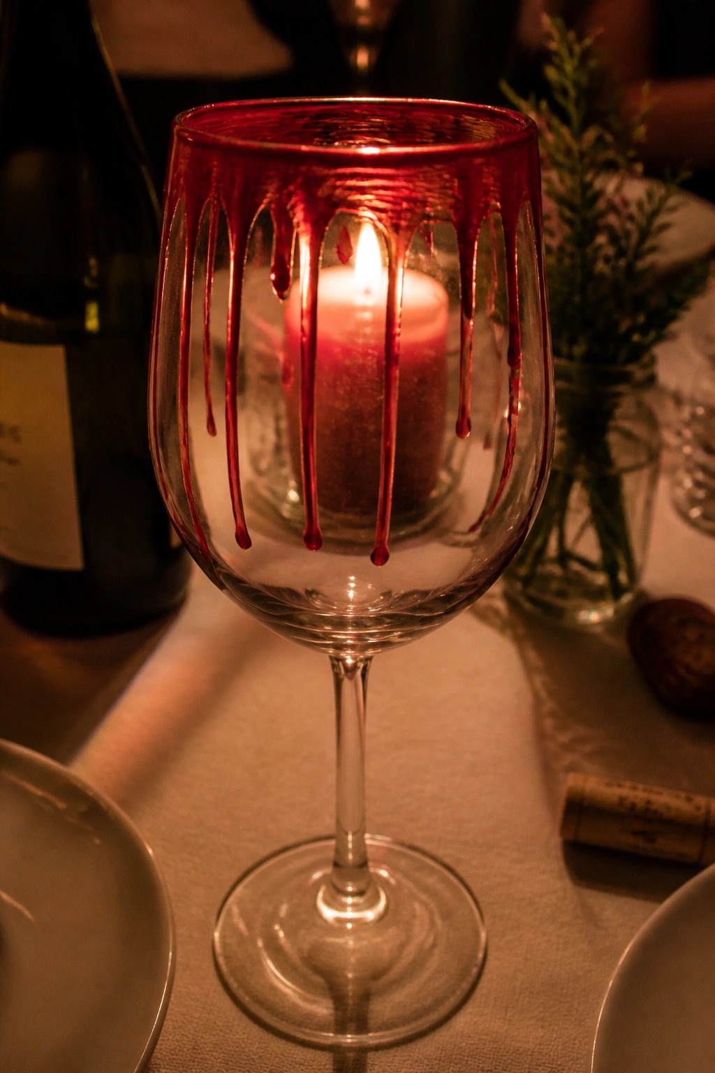 Wine glass with red drips holds a lit glowing candle on table.