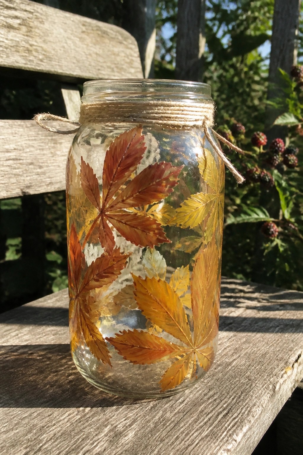 Glass jar decorated with colorful autumn leaves and twine on wooden bench