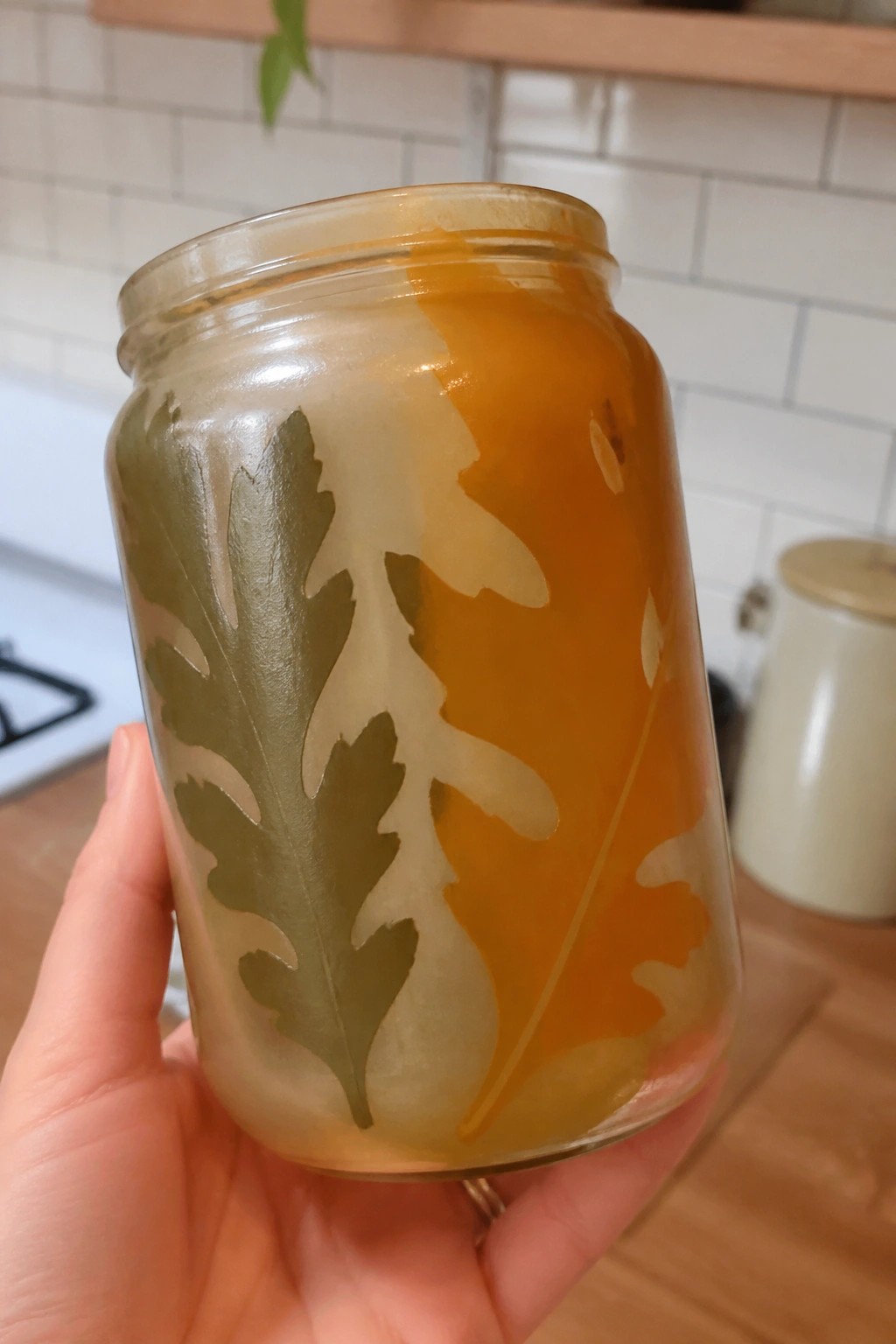 Hand holding glass jar with frosted oak leaf designs and orange liquid
