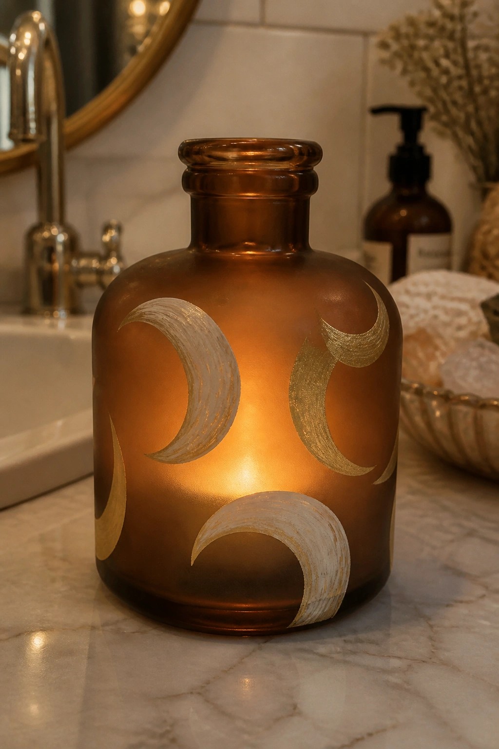 Glowing amber glass bottle with gold crescent moons on marble bathroom counter