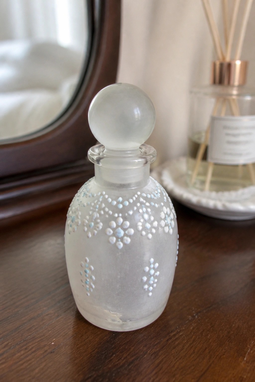 Frosted glass perfume bottle with white and blue dotted patterns on wood