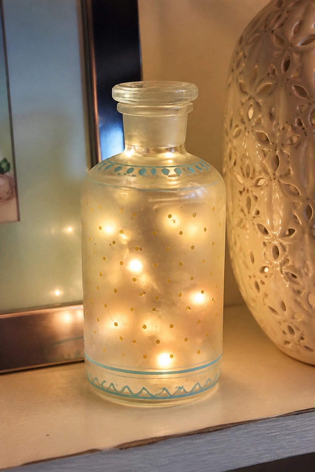 Glowing glass bottle with gold dots and turquoise patterns on wooden shelf
