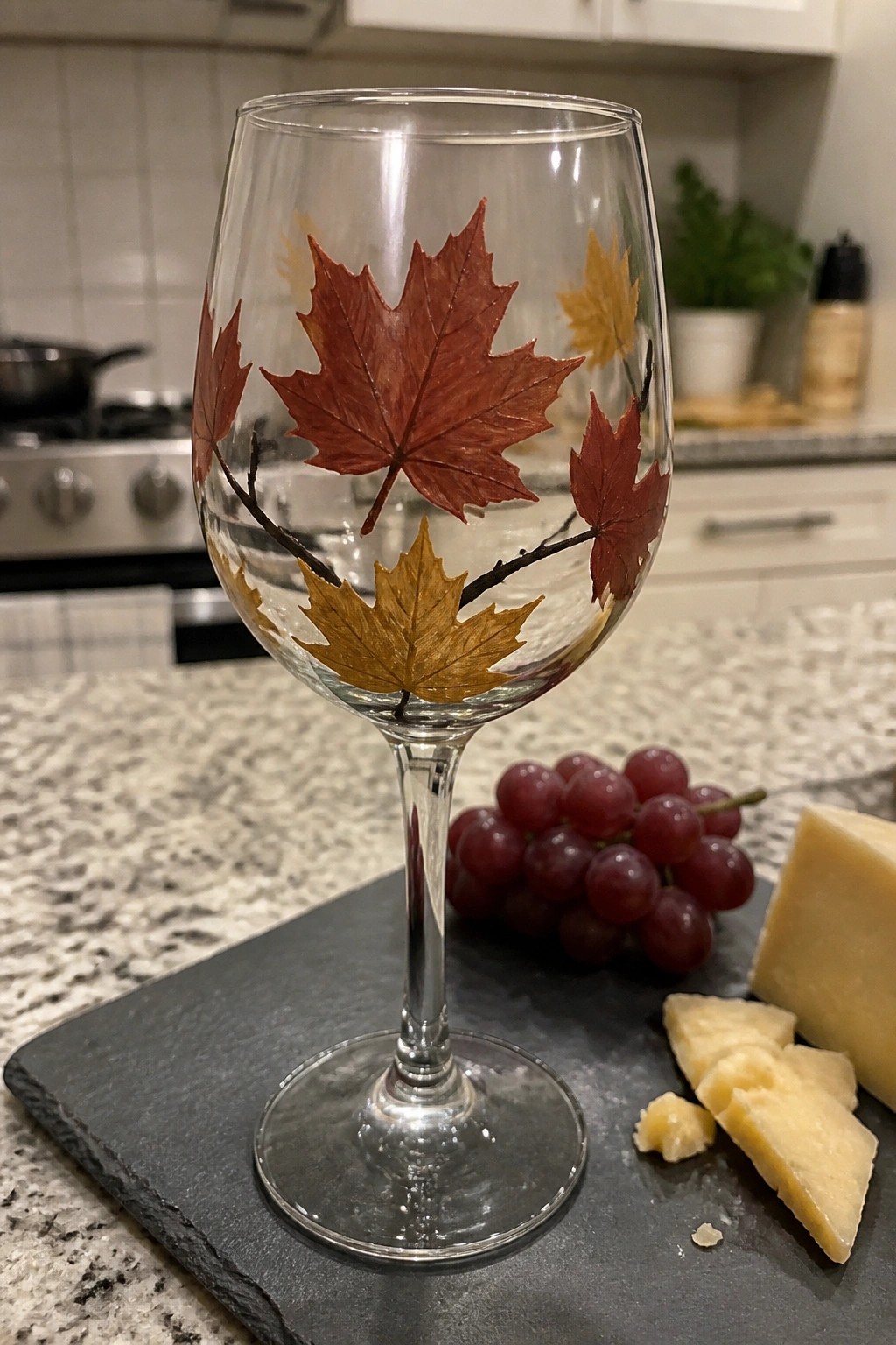 Wine glass with red and yellow autumn leaves beside grapes and cheese on slate.