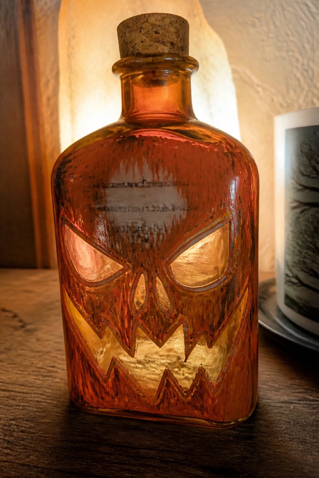 Amber glass bottle with glowing etched jack-o'-lantern face and cork on wood