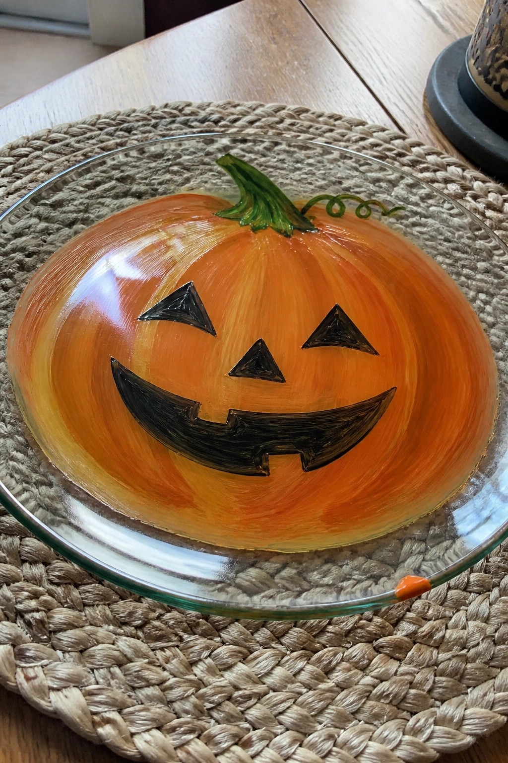 Orange jack-o'-lantern face painted on glass plate atop woven placemat.