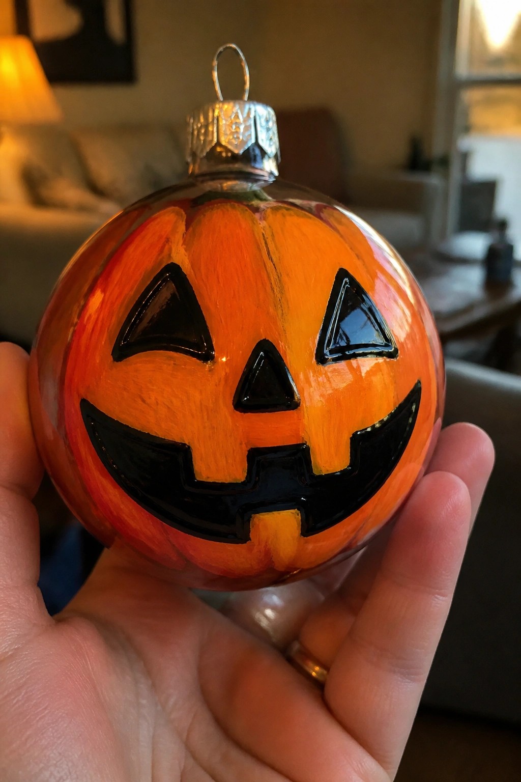 Hand holding shiny glass ornament painted orange as jack-o'-lantern with black face.