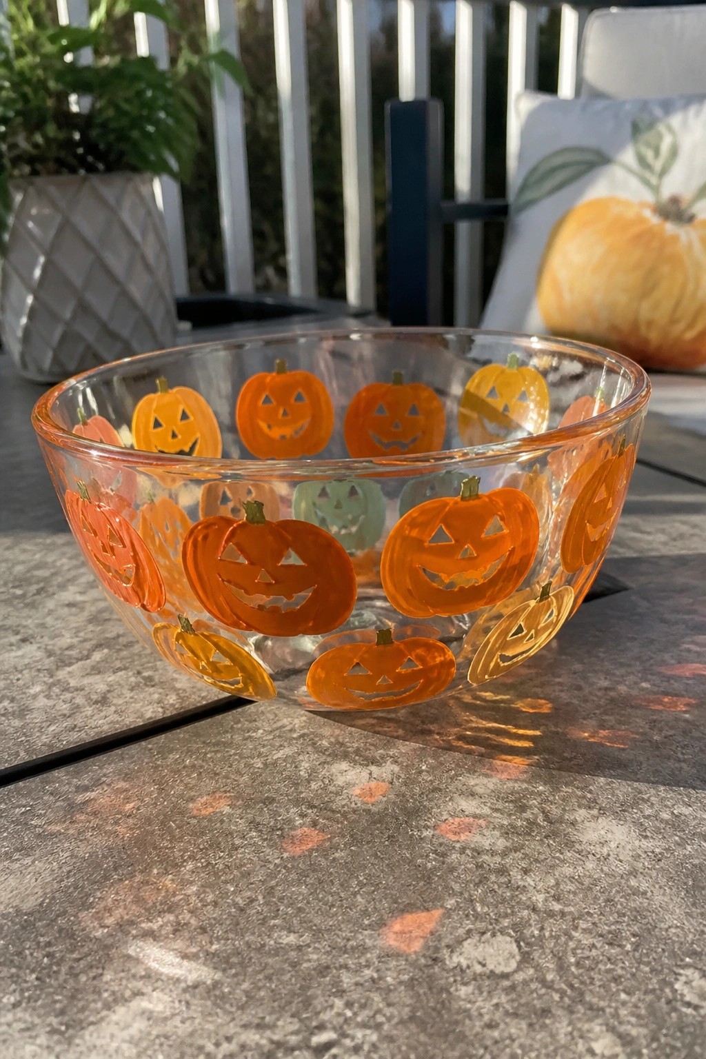 Glass bowl with orange jack-o'-lantern designs on sunny patio table