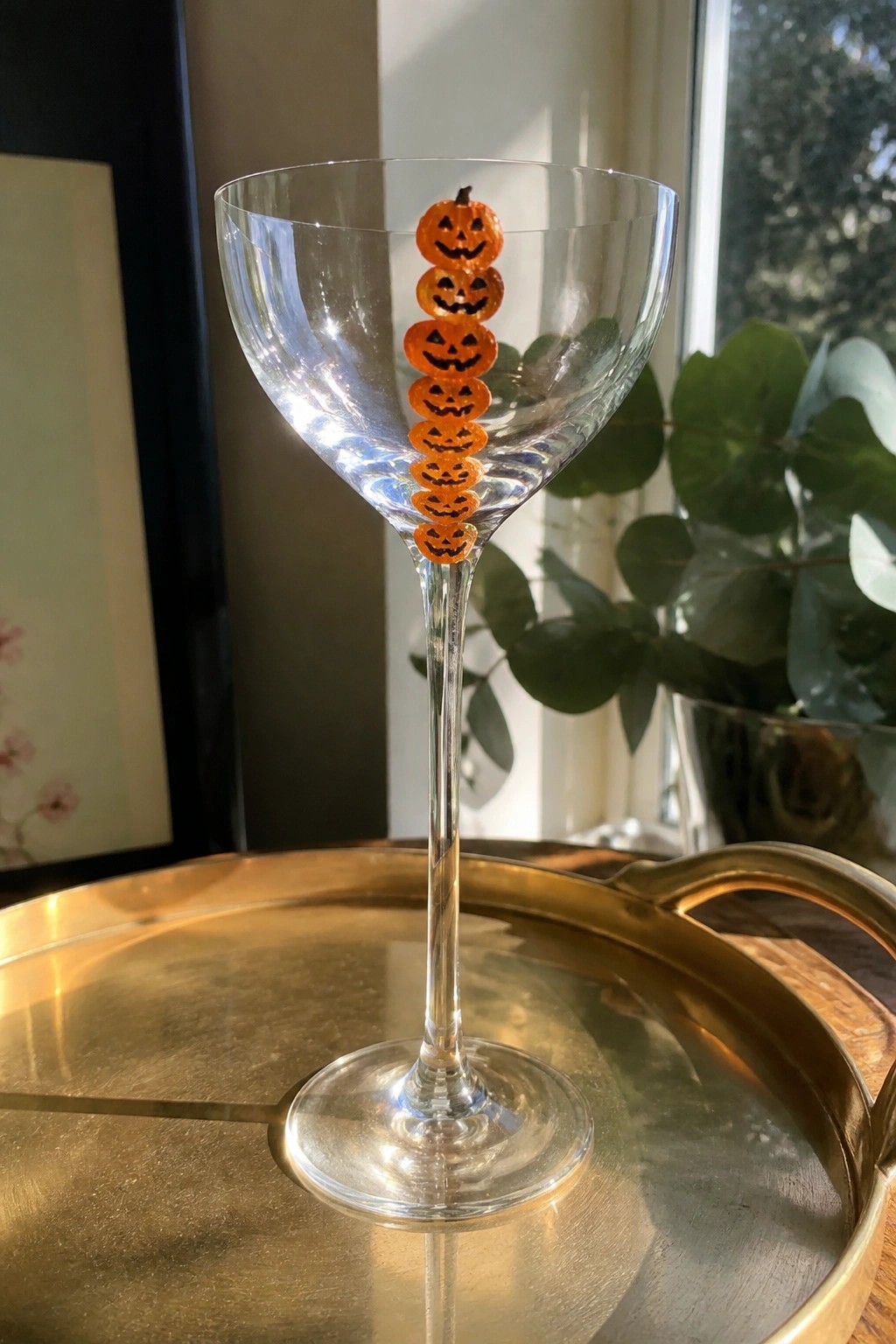 Clear glass with stacked orange jack-o'-lanterns on stem atop golden tray