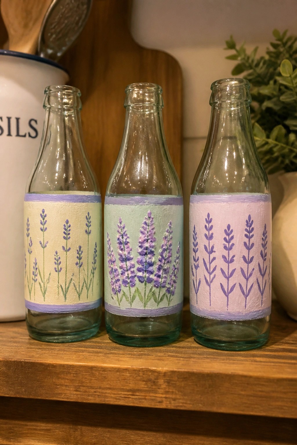 Three glass bottles with pastel lavender paintings on a wooden shelf.