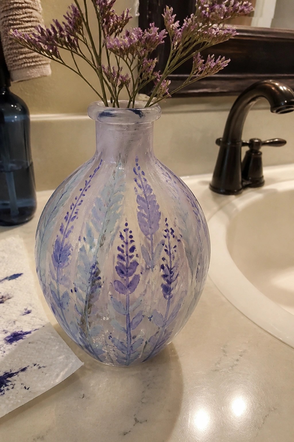 Painted round vase with purple lavender motifs holding flowers on marble bathroom counter