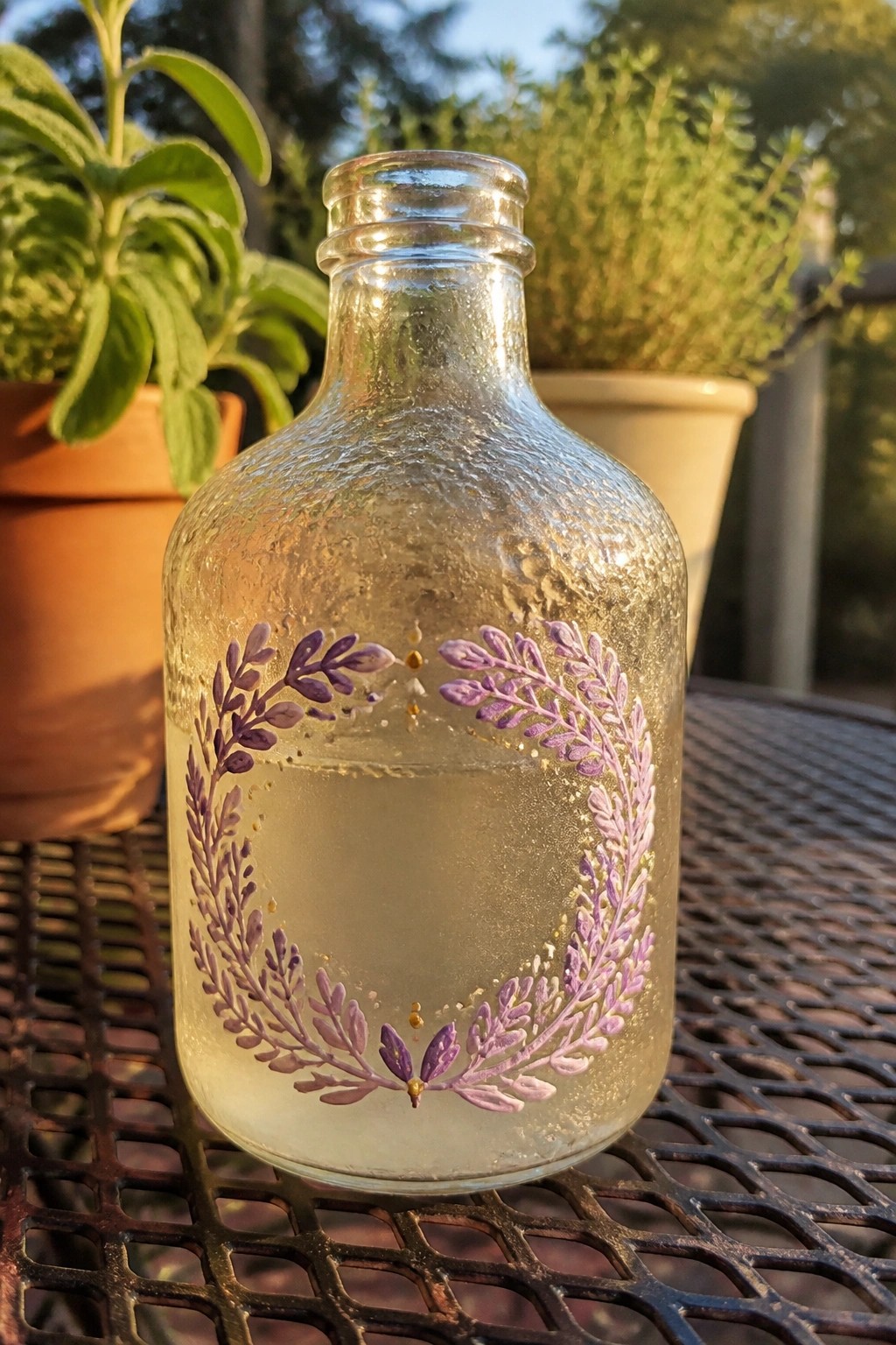 Glass bottle with purple floral wreath and gold dots on metal table outdoors