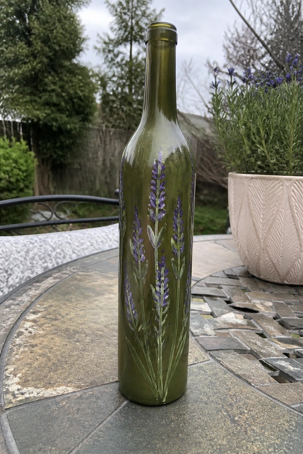 Olive green wine bottle with purple lavender paintings on tiled patio table.