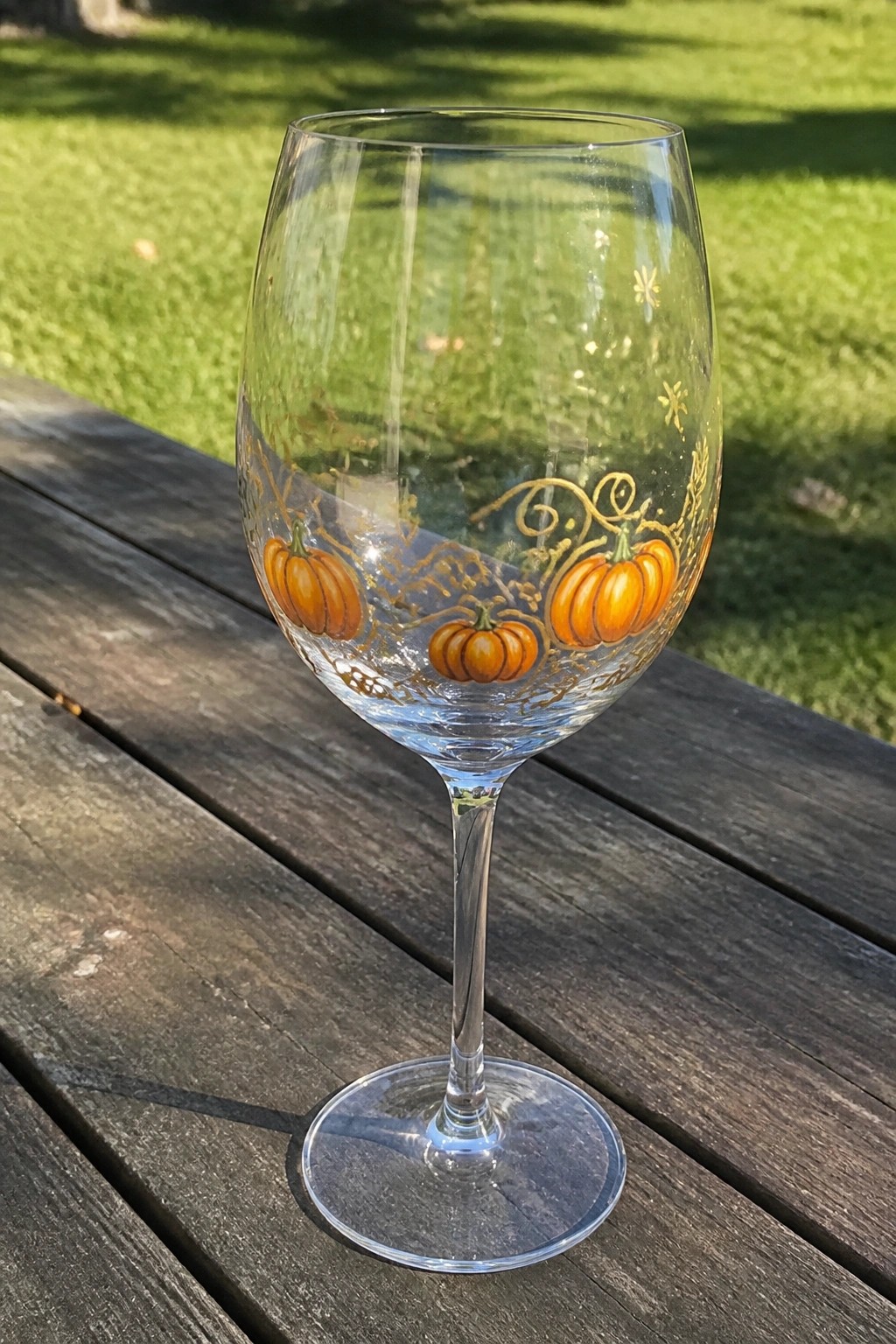 Wine glass painted with orange pumpkins, gold swirls, and stars on wooden table