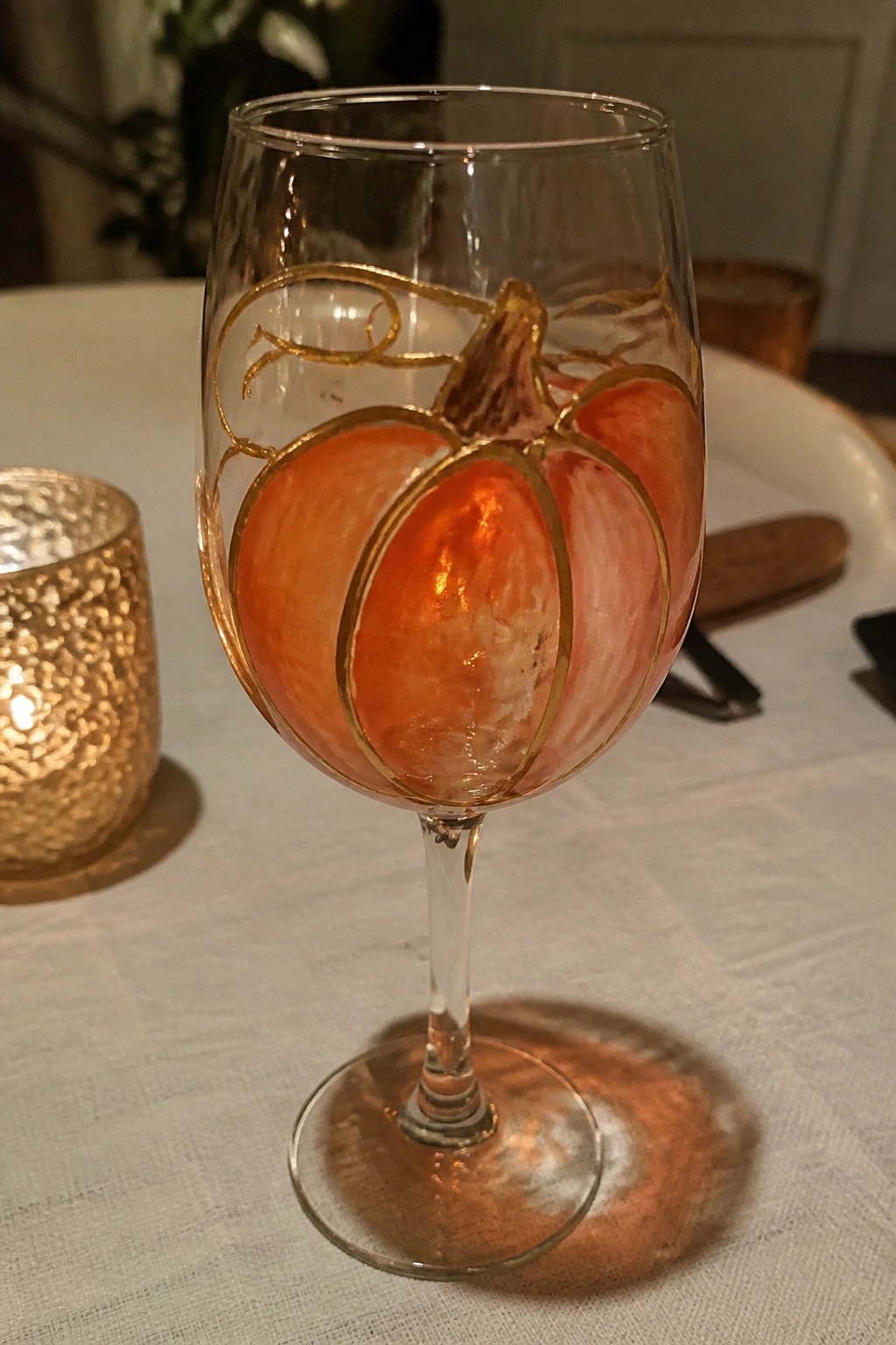 Wine glass with orange pumpkin and gold accents on white tablecloth