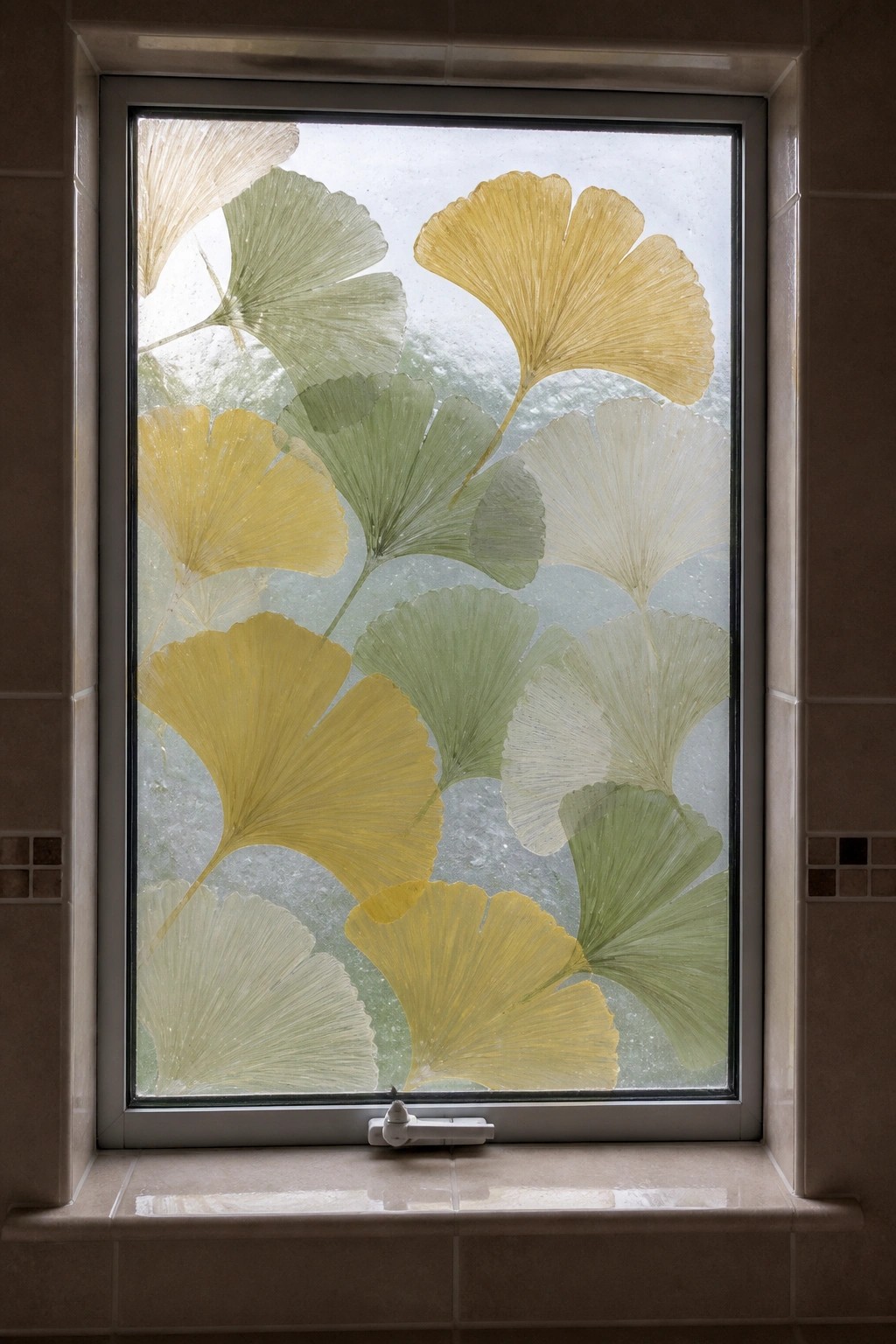 Window with frosted glass and overlapping yellow-green ginkgo leaves on tiled sill