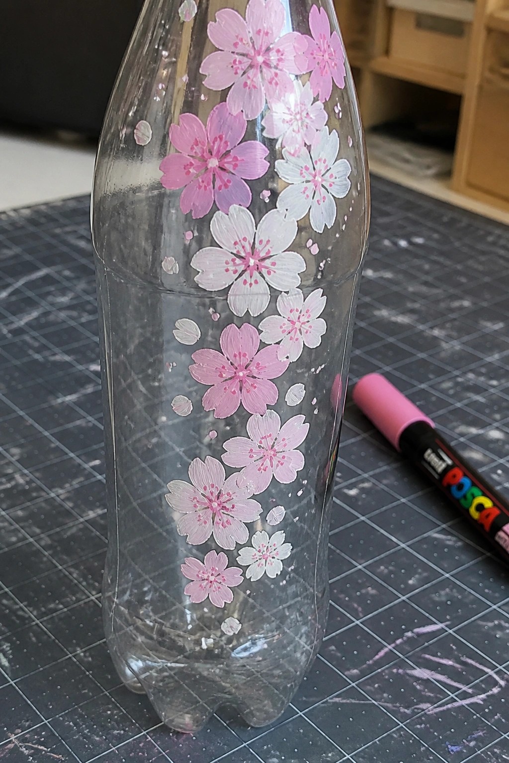 Clear plastic bottle with pink and white cherry blossom paintings beside a Posca marker.