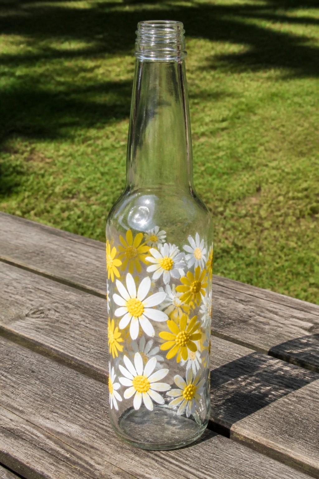 Clear glass bottle with yellow and white daisy decals on wooden outdoor table