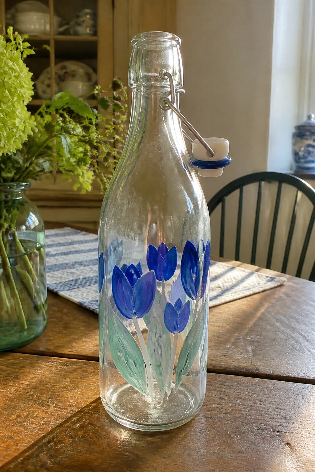 Glass bottle with blue tulips and green leaves, swing-top lid on wooden table