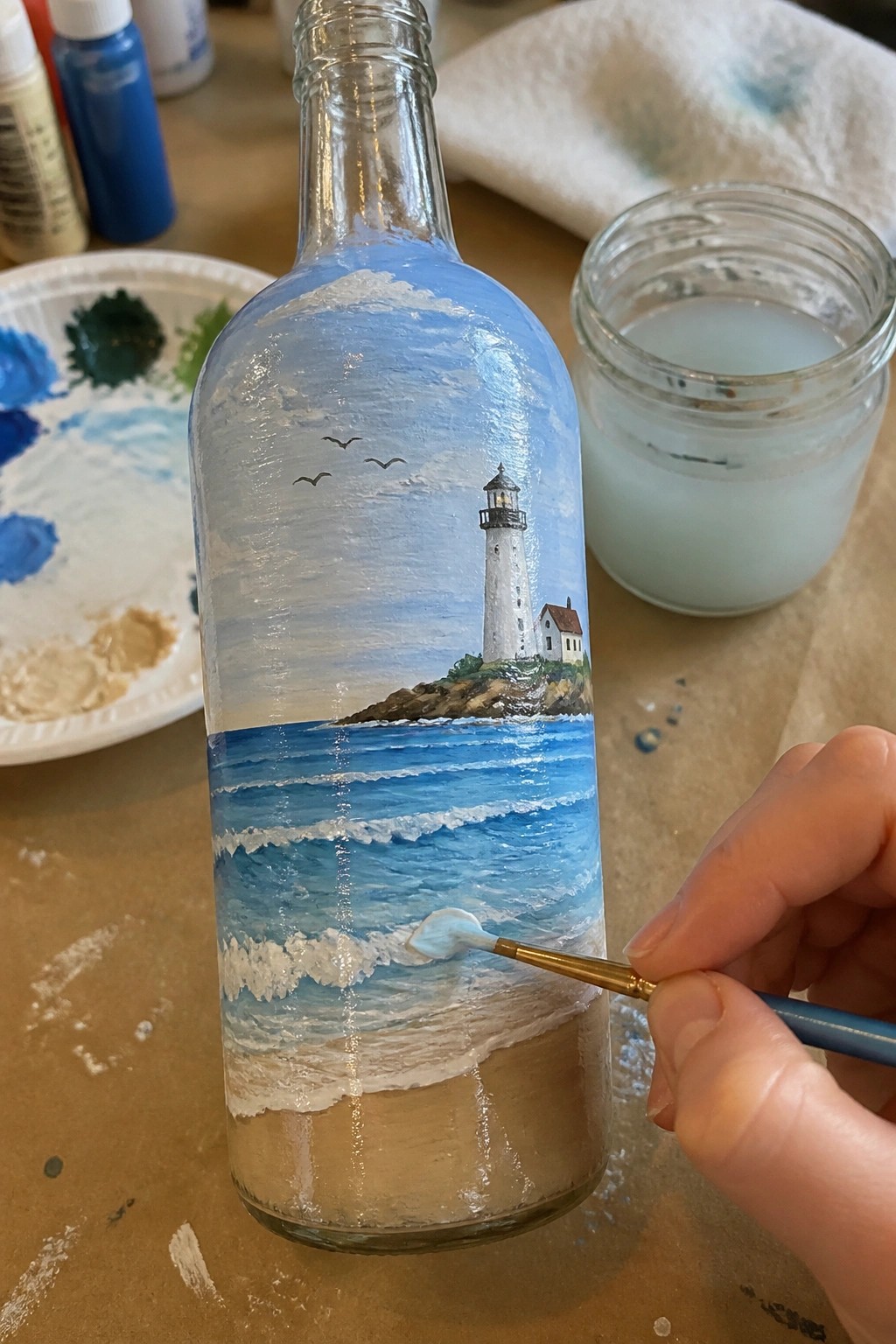 Hand painting white waves on glass bottle with lighthouse ocean scene