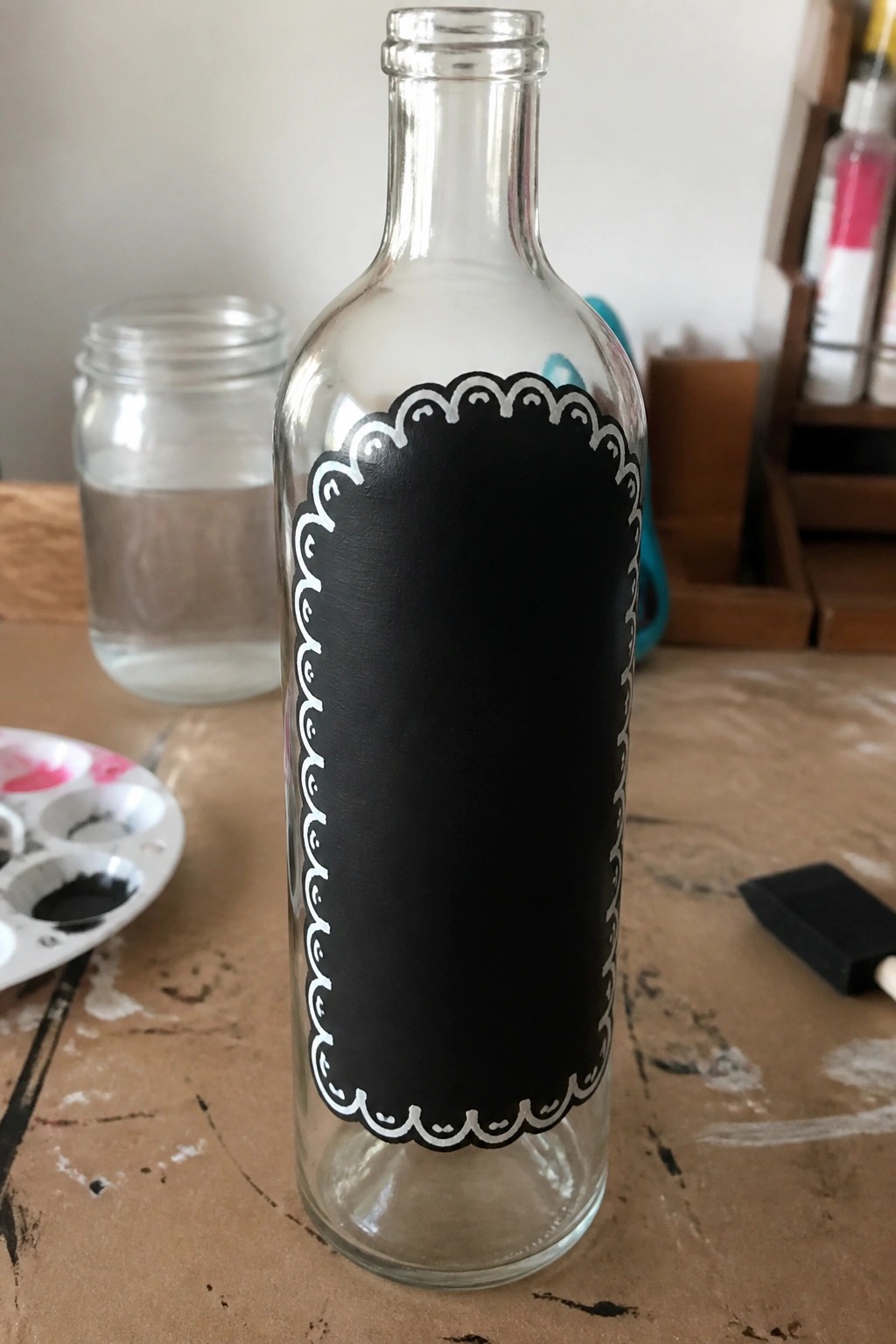 Glass bottle with black chalkboard label and white scalloped border on wooden table