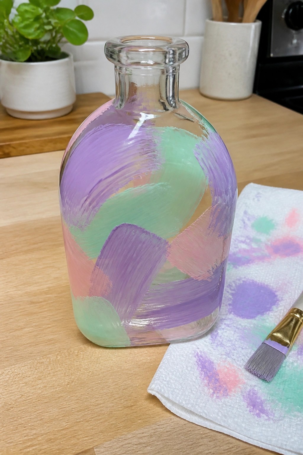 Glass bottle with pastel purple pink green brushstrokes on wooden kitchen counter