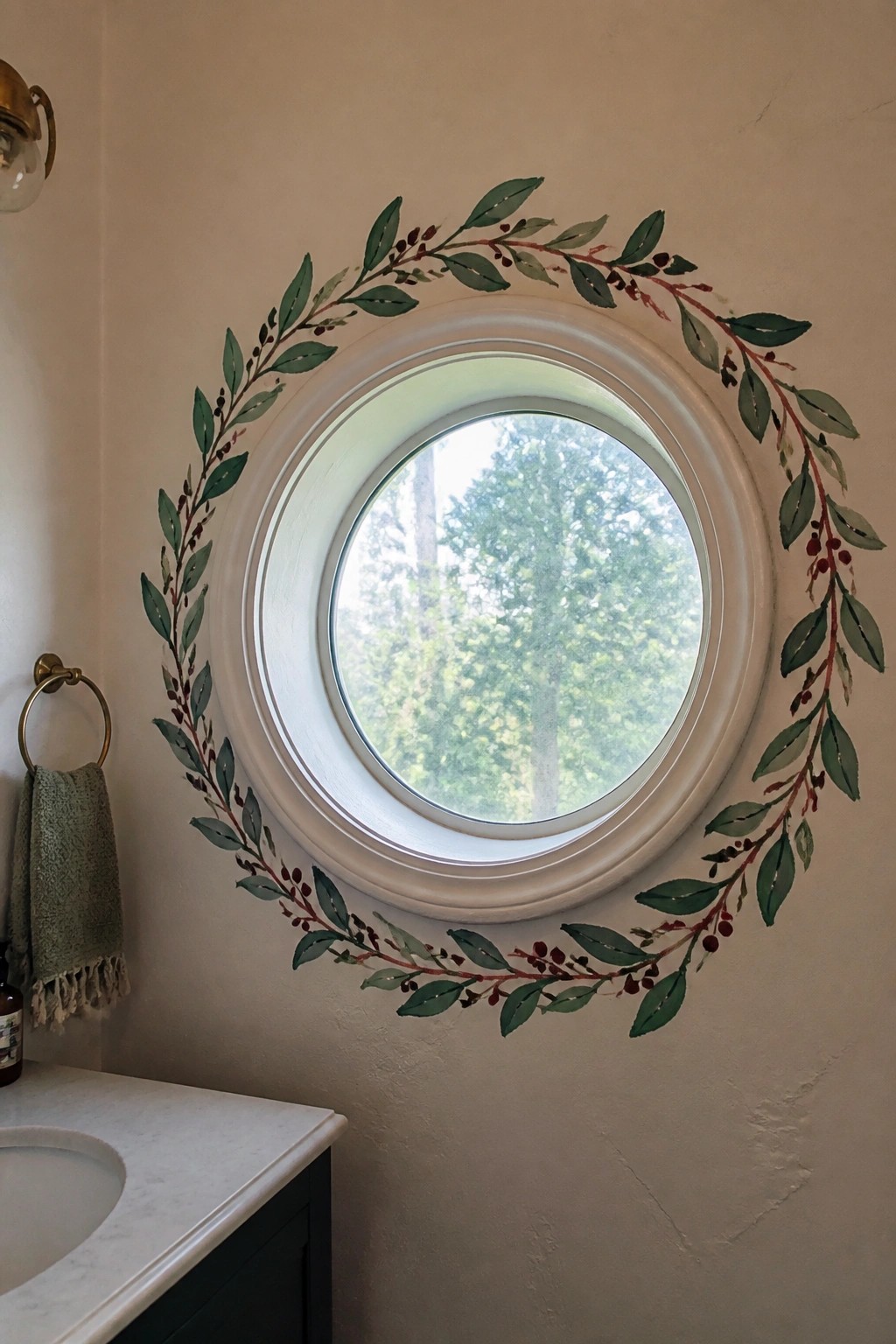 Round window encircled by painted green leaves and red berry wreath in bathroom