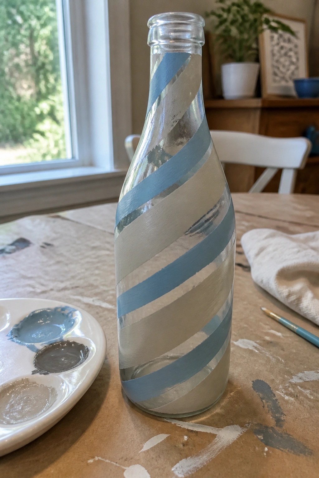 Glass bottle with blue and white spiral stripes on wooden table near paint palette