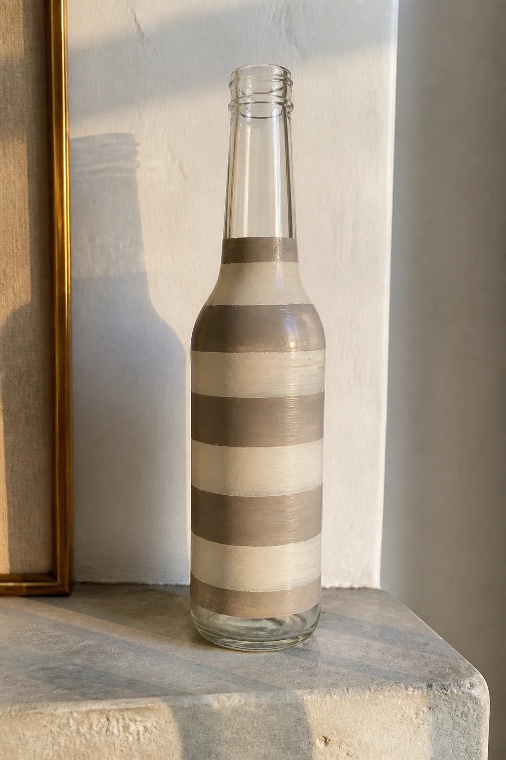 Glass bottle with horizontal gray and beige stripes on a stone ledge