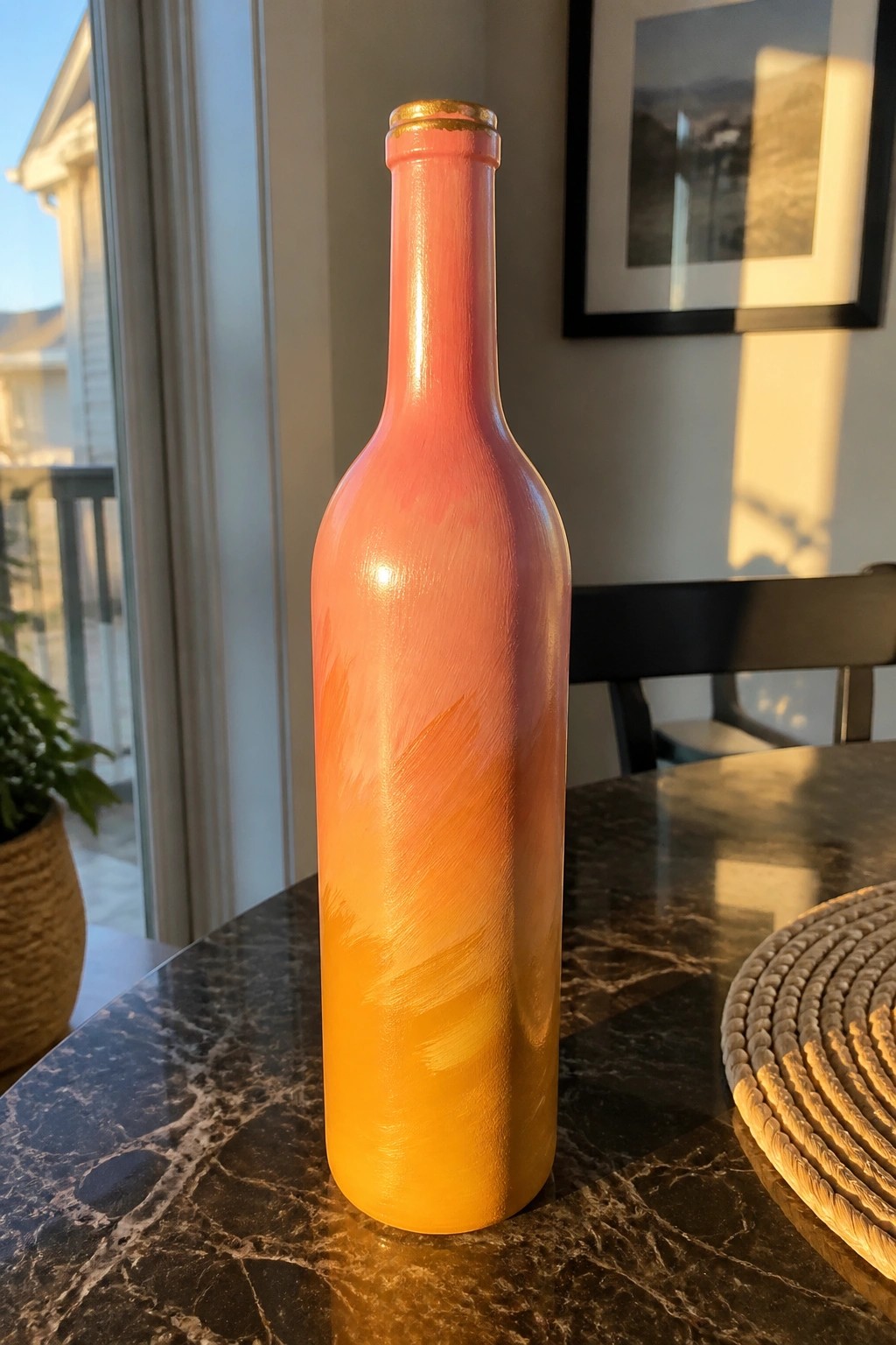 Gradient painted bottle from pink to orange with gold neck on marble table
