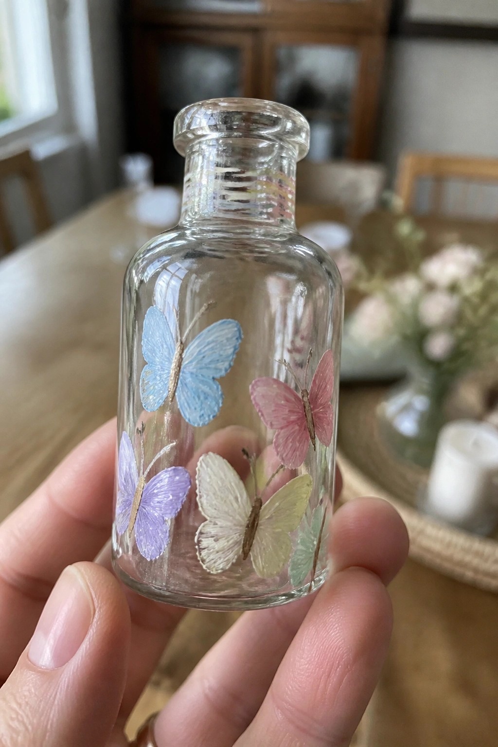 Hand holding clear glass bottle painted with colorful butterflies in blue, pink, and purple.