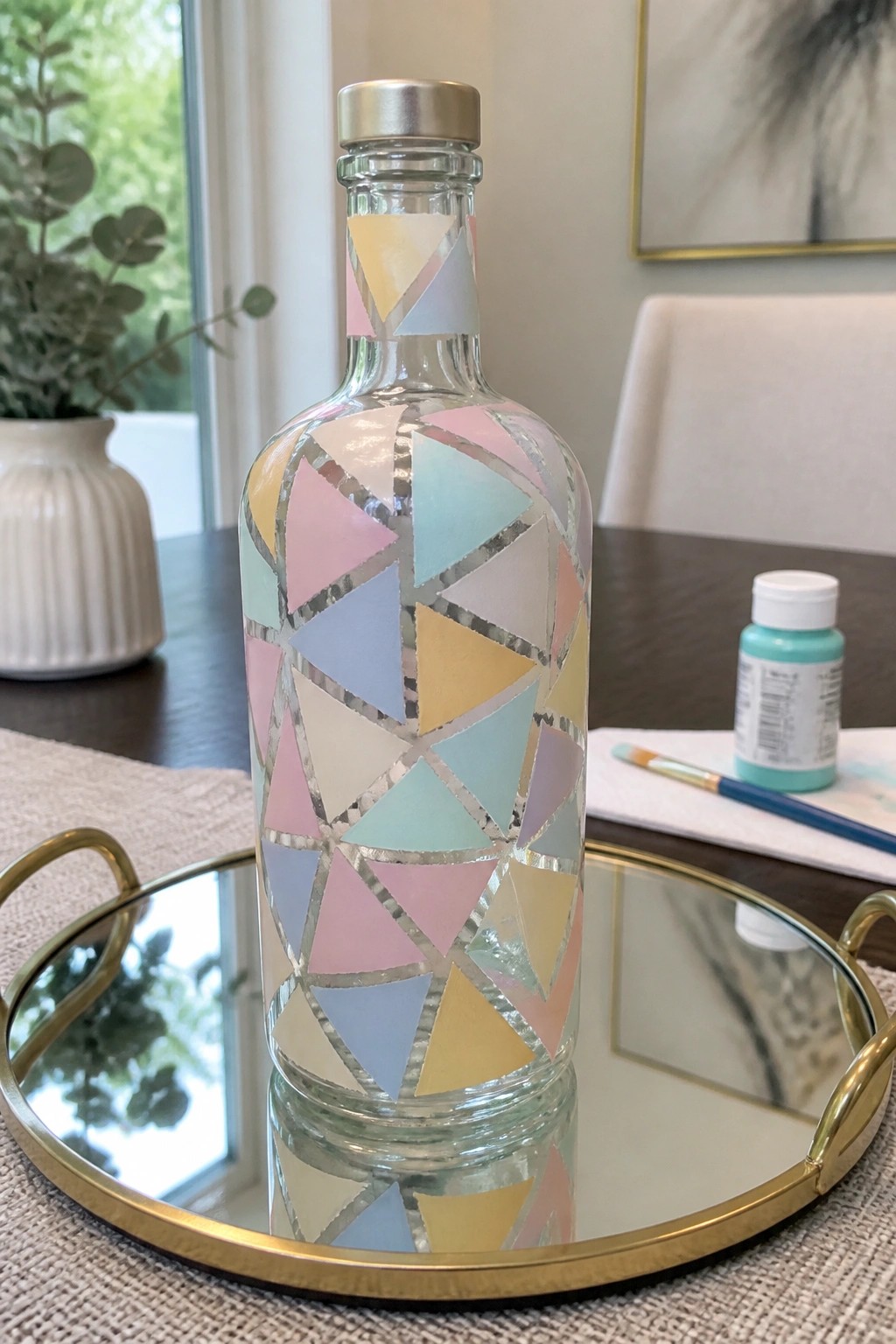 Pastel triangular mosaic covers a glass bottle on a gold mirror tray