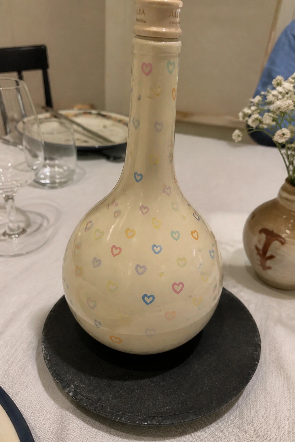 Cream bottle with colorful hearts on black plate atop dining table with glasses