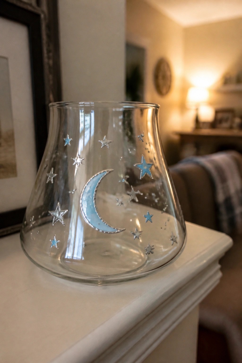 Glass candle holder with blue crescent moon and silver stars on white ledge