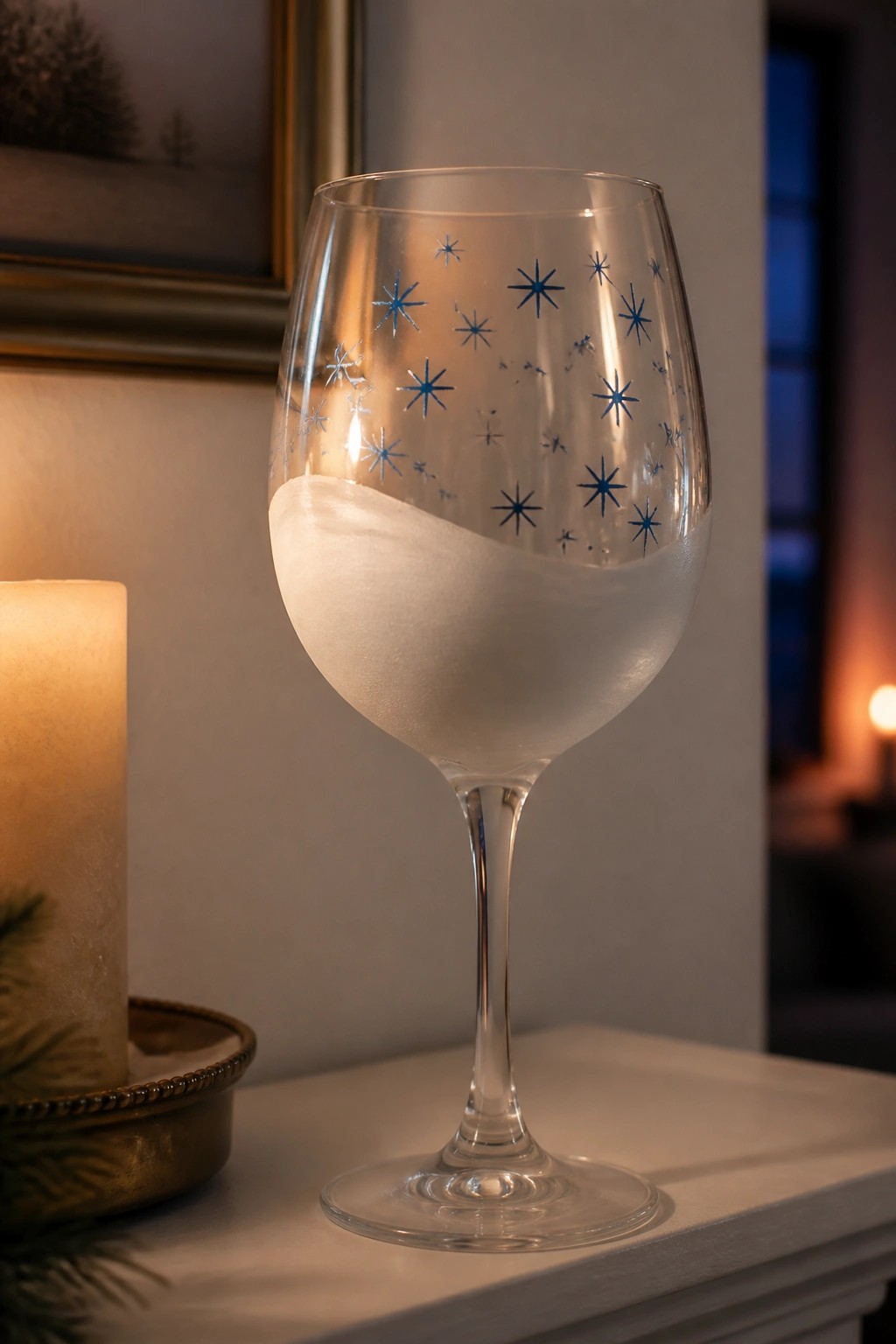 Wine glass with blue star patterns and frosted white base beside lit candle.