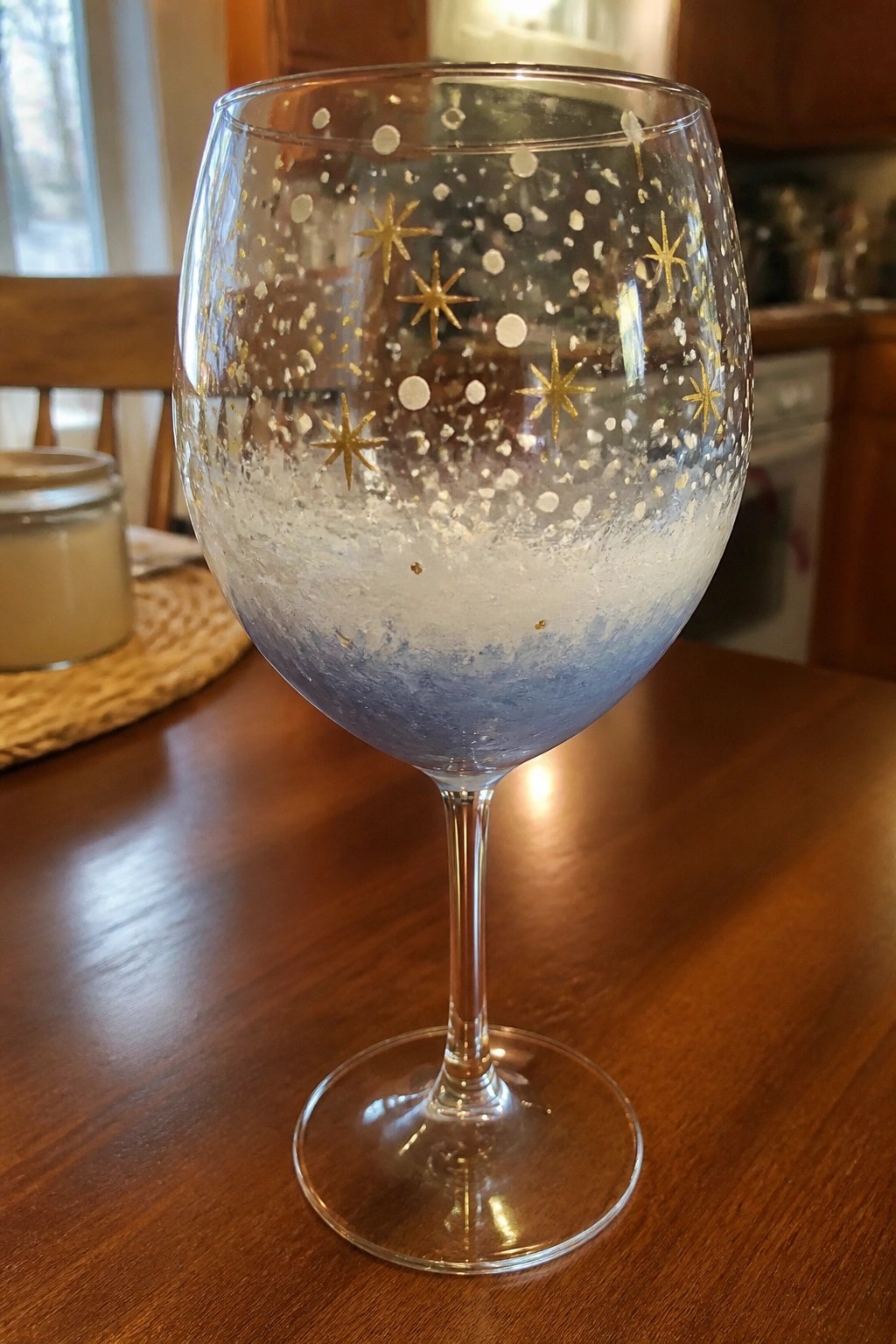 Decorated wine glass with blue gradient base, gold stars, and white dots on wooden table.