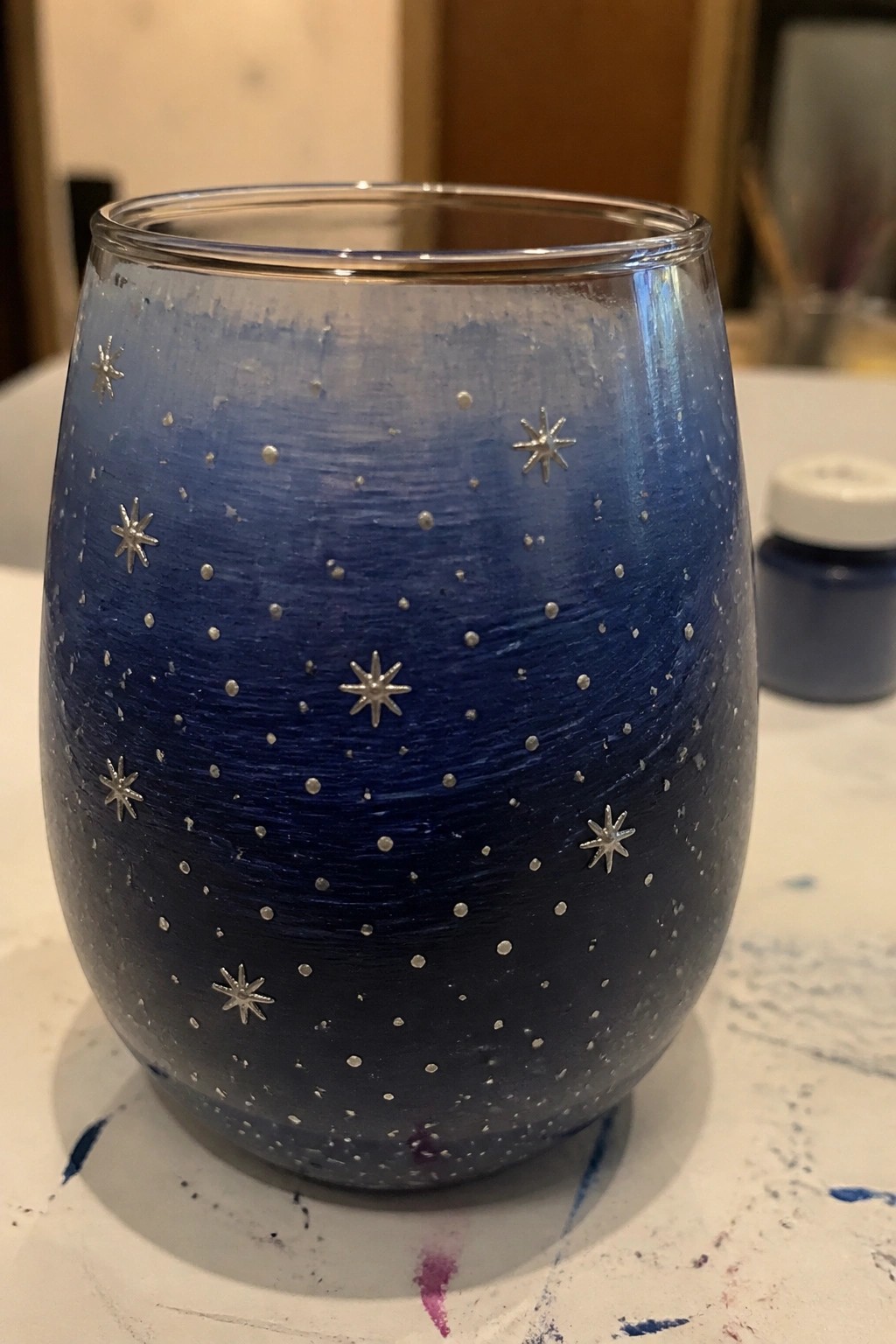 Blue painted glass tumbler with silver stars on paint-splattered surface