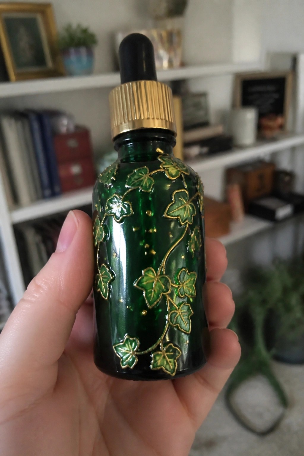 Hand holding dark green dropper bottle with gold ivy leaf designs