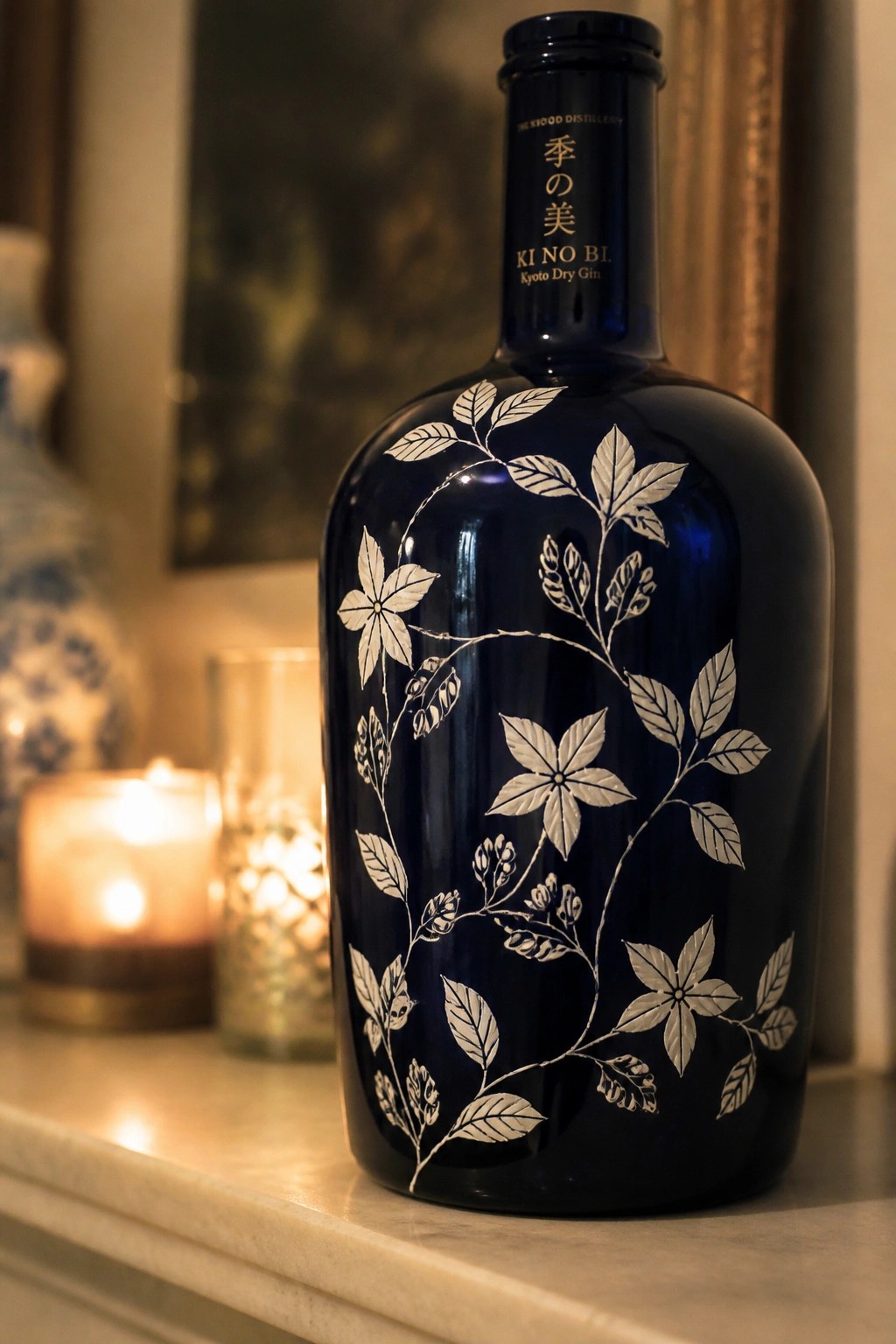 Dark blue Kyoto Dry Gin bottle with white floral vine engravings beside lit candle