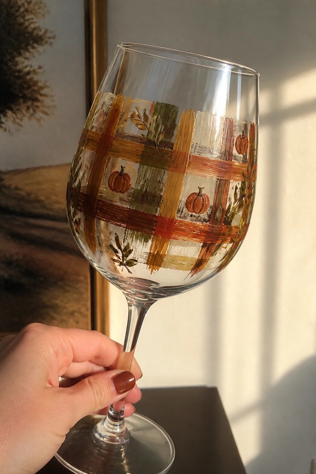 Hand holding wine glass hand-painted with plaid, pumpkins, and autumn leaves