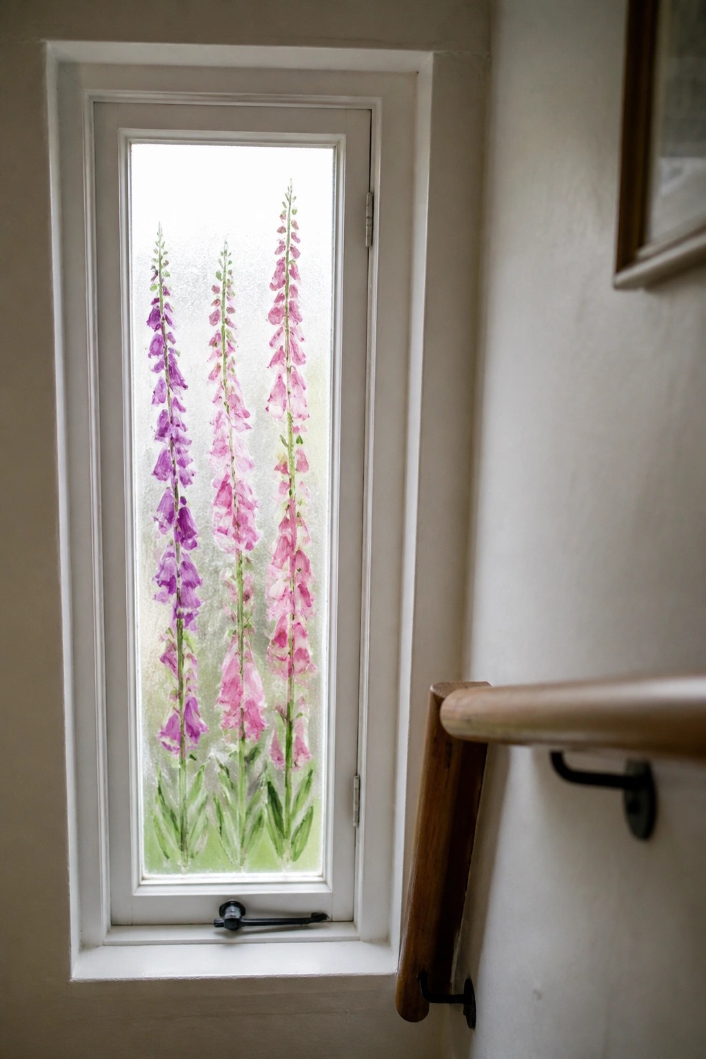 Narrow window with pink and purple foxgloves painted on frosted glass beside wooden handrail